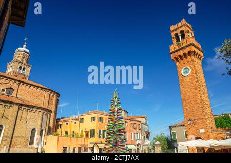 Murano, Italien, 14. September 2019: Uhrenturm Torre dell'Orologio, Kirche San Pietro Martyre und bunten weihnachtsbaum aus Murano-Glas auf Campo Santo Stefano Platz auf Murano-Inseln Stockfoto