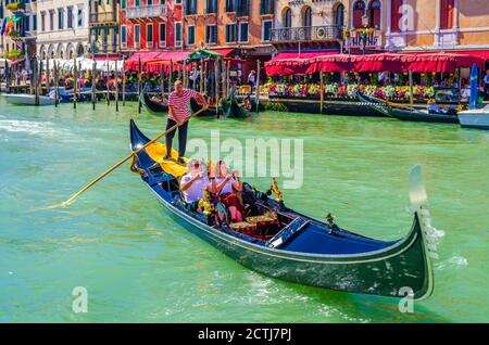 Venedig, Italien, 13. September 2019: Gondoliere und Touristen auf Gondel traditionelle Boot Segeln auf dem Wasser des Canal Grande Wasserstraße mit venezianischer Architektur typischen bunten Gebäuden Hintergrund Stockfoto
