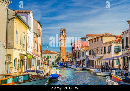 Murano-Inseln mit Uhrturm Torre dell'Orologio, Boote und Motorboote in Wasserkanal, bunte traditionelle Gebäude, Lagune von Venedig, Region Venetien, Norditalien. Murano Postkarte Stadtbild. Stockfoto