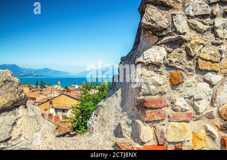 Blick auf das historische Zentrum Desenzano del Garda Altstadt, See und Bergkette durch Merlons von Backstein zerstörte Mauer der mittelalterlichen Burg, blauer Himmel Kopieplatz, Lombardei, Norditalien Stockfoto