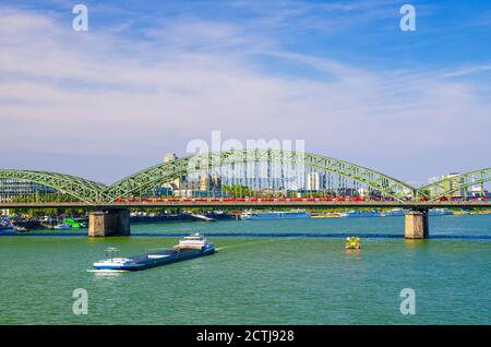 Die Hohenzollernbrücke oder Hohenzollernbrücke über den Rhein mit auf dem Wasser fahrenden Frachtschiffen, Fußgänger- und Eisenbahnstahlbrücke, Köln-Zentrum, Nordrhein-Westfalen, Deutschland Stockfoto