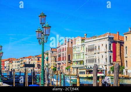 Pier Dock mit hölzernen Pfosten des Canale Grande Wasserstraße im historischen Stadtzentrum von Venedig mit Reihe von bunten Gebäuden venezianische Architektur, Möwen in blauem Himmel. Region Venetien, Norditalien. Stockfoto