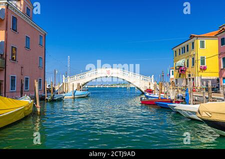 Steinbrücke Ponte di Vigo über den Kanal von Vena mit bunten Booten und alten Gebäuden im historischen Zentrum der Stadt Chioggia, blauer Himmel im Sommer, Region Venetien, Norditalien Stockfoto