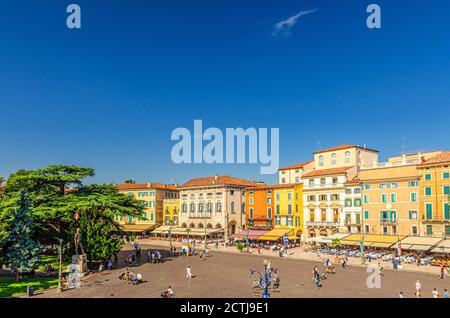 Verona, Italien, 12. September 2019: Piazza Bra Platz im historischen Stadtzentrum mit Reihe von alten bunten bunten Gebäuden Cafés und Restaurants, grüne Bäume und Wandertouristen, blauer Himmel Stockfoto