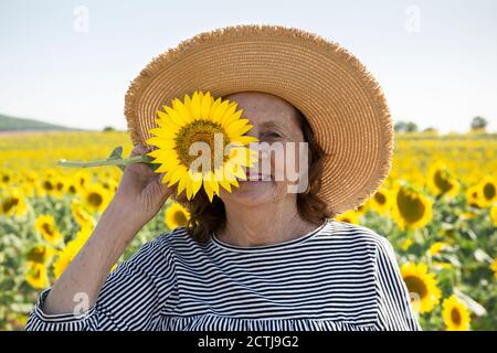 Porträt einer älteren Frau mit einer Sonnenblume auf ihrem Gesicht. Sie ist draußen. Stockfoto