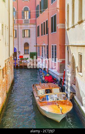 Venedig Stadtbild mit schmalem Wasserkanal mit Gondel und Yacht Boot zwischen alten Gebäuden im historischen Stadtzentrum, Venetien Region, Norditalien vertäut. Typisch venezianischer Blick, vertikale Ansicht Stockfoto