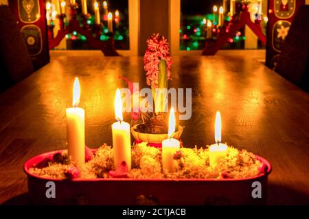 Brennende Adventskerzen, roter Kerzenständer, Eichentisch, Ansicht schließen Heiligabend. Traditionelle Dekoration im schwedischen Haus mit Fensterbeleuchtung, Hyazinthe Flo Stockfoto