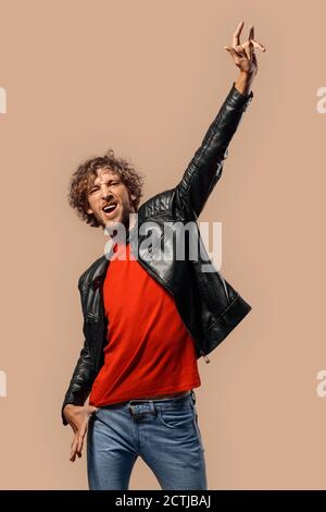 Freistil. Mann mit lockigen Haaren in Laserjacke isoliert auf Gras Hand neben Hörnern Geste schreien cool stehen Stockfoto