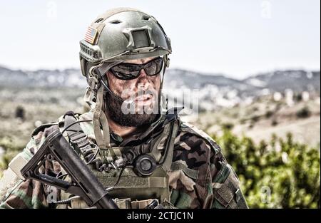 Schulterportrait des Soldaten, Spezialeinsatzkämpfers, moderner Kampfkämpfer mit schmutzigem, unrasierten Gesicht, Sonnenbrillen, Kampfhelm und Sprechern im taktischen Radio-Headset während der Mission Stockfoto
