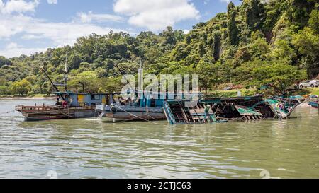 Ein halb eingetauchtes Fischerboot und zwei weitere Holzboote im Pukat Village, einem Fischerdorf an der Jalan Bokara im Süden von Sandakan. Stockfoto