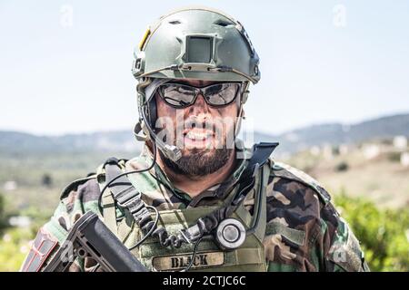 Schulterportrait des Soldaten, Spezialeinsatzkämpfers, moderner Kampfkämpfer mit schmutzigem, unrasierten Gesicht, Sonnenbrillen, Kampfhelm und Sprechern im taktischen Radio-Headset während der Mission Stockfoto