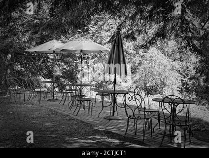 Eine Reihe von Metallstühlen, Tischen und Sonnenschirmen im Freien erstreckt sich über die Länge einer gemauerten Terrasse über einem hell erleuchteten Tal und dem Concord River. Stockfoto