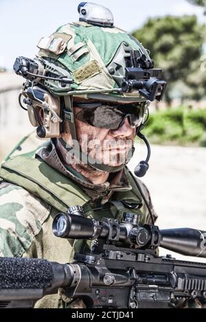 Schulterportrait des Soldaten, Spezialeinsatzkämpfers, moderner Kampfkämpfer mit schmutzigem, unrasierten Gesicht, Sonnenbrillen, Kampfhelm und Sprechern im taktischen Radio-Headset während der Mission Stockfoto