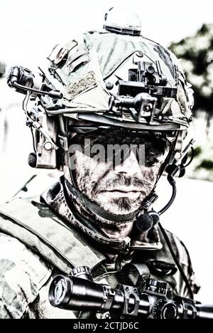 Schulterportrait des Soldaten, Spezialeinsatzkämpfers, moderner Kampfkämpfer mit schmutzigem, unrasierten Gesicht, Sonnenbrillen, Kampfhelm und Sprechern im taktischen Radio-Headset während der Mission Stockfoto