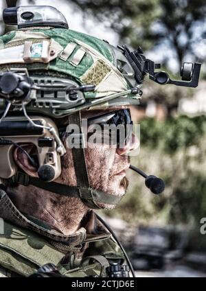 Schulterportrait des Soldaten, Spezialeinsatzkämpfers, moderner Kampfkämpfer mit schmutzigem, unrasierten Gesicht, Sonnenbrillen, Kampfhelm und Sprechern im taktischen Radio-Headset während der Mission Stockfoto