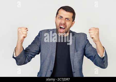 Junger Geschäftsmann Mann mit einem Bart wütend und verrückt, seine Fäuste, frustriert und wütend, schreien vor Wut. Wut und aggressives Konzept. Porträt eines Mannes auf grauem Hintergrund. Stockfoto