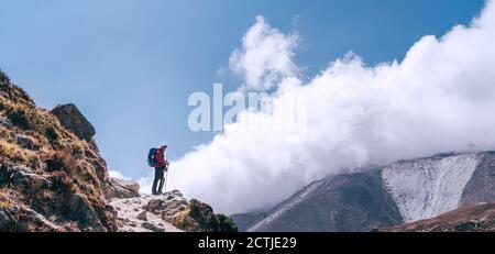 Wanderer Mann Silhouette auf Wolken Hintergrund stehend auf Pfad über das Imja Khola Tal und genießen Sie die Aussicht auf die Berge während eines Everest Base Camp tr Stockfoto