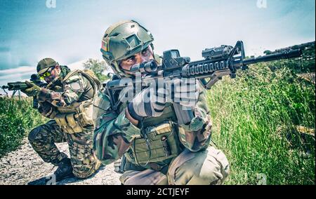 Armeesoldaten, versiegelt Mannschaftskämpfer in voller Munition, Ziel Sturmgewehr mit Kollimator Anblick, kniend im Gras, einander bedecken, Bereich beobachten, Mähen auf feindlichem Gebiet Stockfoto