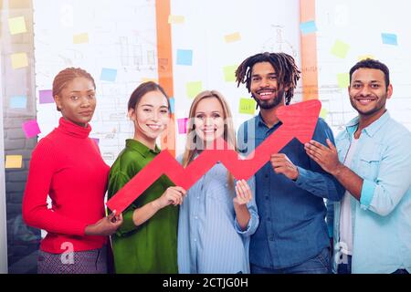 Junge fröhlich-bunten Business Team eine rote statistische Pfeil gedrückt halten. Konzept der wachsenden, erfolgreichen und Gewinn Stockfoto