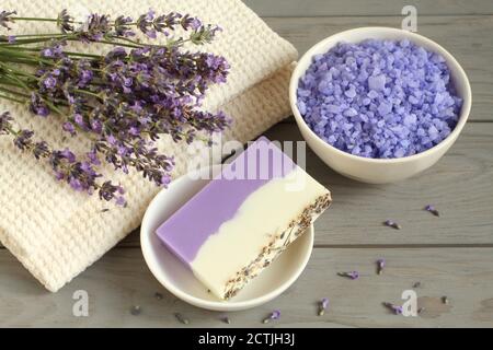 Meersalz mit Lavendel in einer weißen Schüssel, Seife aus Lavendel, Olivenöl und Kakaobutter auf einem weißen Teller und Lavendelblüten auf einem Leinentücher ar Stockfoto