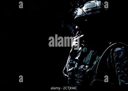Armee Soldat in Kampfuniform und Helm, Rauchen Zigarette in der Dunkelheit. Special Operations Forces Kämpfer, ruhende Infantryman Silhouette mit Zigarette im Mund und Tabakrauch, Low-Key Stockfoto
