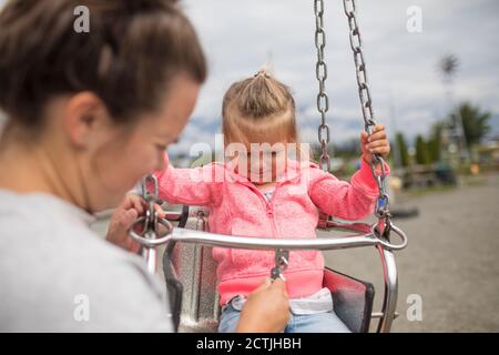 Mutter knickende Tochter in Schaukelfahrt. Stockfoto