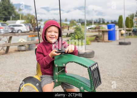 Junge sitzt auf Spiel Fahrt auf Traktor auf Bauernhof gemacht Aus recycelten Reifen Stockfoto