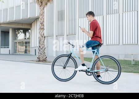 Junger Mann mit Beinprothese sitzt auf dem Fahrrad und Messaging Auf dem Smartphone in der Stadt Stockfoto