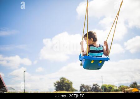 Low-Angle-Ansicht des Jungen schwingen im Freien auf blauen Schaukel auf dem Spielplatz. Stockfoto