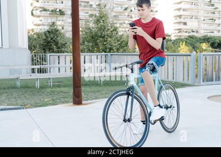 Junger Mann mit Beinprothese sitzt auf dem Fahrrad und Messaging Auf dem Smartphone in der Stadt Stockfoto