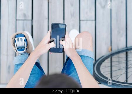 Männlicher Radfahrer mit Beinprothese sitzt auf der Bank und mit Mobiltelefon Stockfoto