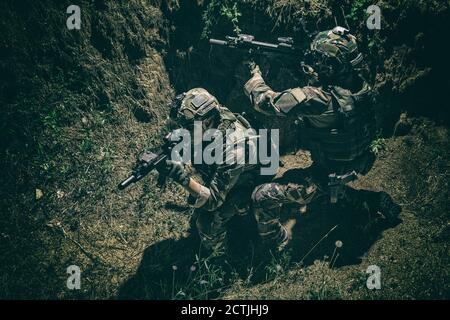 Zwei Soldaten der Armee, Navy siegelt Team Schützen tragen Kampfuniform, Körperpanzerung und Helm, zielende Service Gewehre, die sich gegenseitig während der Bewegung in Graben. Infanteristen auf dem Schlachtfeld bei Nacht Stockfoto