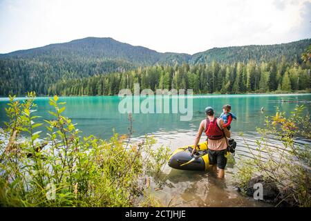 Vater trägt Sohn durch Wasser in aufblasbare Boot, Vater Sohn Reise Stockfoto