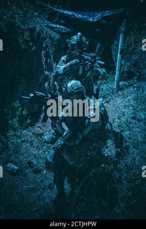 Zwei Soldaten der Armee, Navy siegelt Team Schützen tragen Kampfuniform, Körperpanzerung und Helm, zielende Service Gewehre, die sich gegenseitig während der Bewegung in Graben. Infanteristen auf dem Schlachtfeld bei Nacht Stockfoto