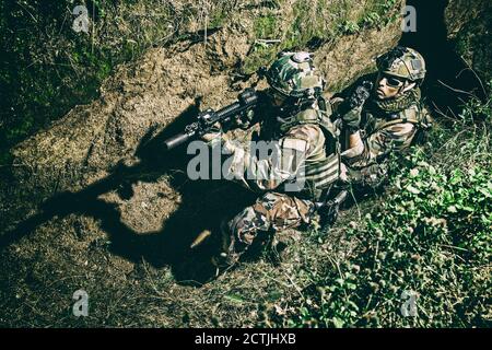 Zwei Soldaten der Armee, Navy siegelt Team Schützen tragen Kampfuniform, Körperpanzerung und Helm, zielende Service Gewehre, die sich gegenseitig während der Bewegung in Graben. Infanteristen auf dem Schlachtfeld bei Nacht Stockfoto