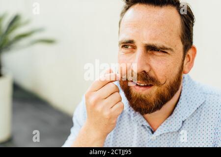 Bärtiger Kaukasianer mit Sommersprossen, die seinen Schnurrbart berühren Stockfoto