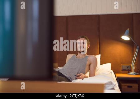 Fröhlicher Kerl, der auf dem Bett liegt und sich einen Film im Fernsehen ansieht Abends zu Hause Stockfoto
