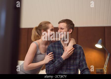 Junge Frau umarmt glücklich Freund, während auf dem Bett im sitzen Abend zusammen Stockfoto
