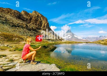 Frau mit Schweizer Flagge am Matterhorn oder Monte Cervino oder Mont Cervin, reflektiert am Riffelsee. Tourismus in Zermatt, Kanton Wallis Stockfoto