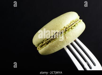 Einzelner grüner Makronen- oder Makronen-Kuchen auf einer Gabel auf schwarzem Hintergrund. Seitenansicht, Nahaufnahme, Makro. Stockfoto