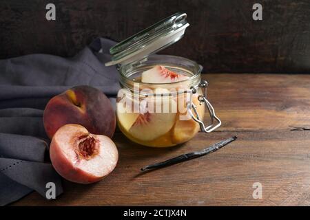 Pfirsiche, frisch und in einem Glas mit Vanille konserviert, um im Winter Früchte aus der Dose, blaue Serviette und dunkles rustikales Holz, Kopierraum, ausgewählter Fokus haben Stockfoto