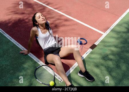 Weibliche Tennisspielerin mit geschlossenen Augen, die sich auf dem Boden entspannt Sportplatz Stockfoto