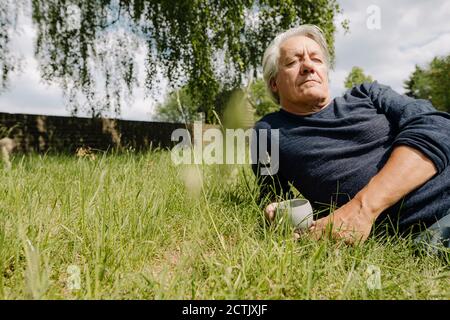 Betrachtend Mann mit Tasse liegend auf Seite über Gras in Hinterhof Stockfoto