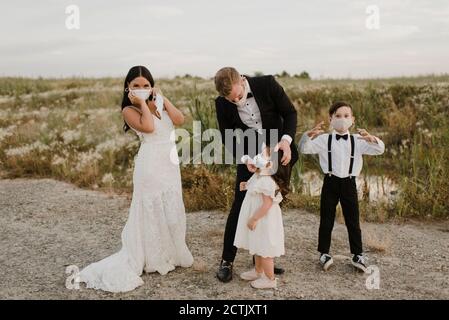 Eltern mit Kindern im Hochzeitskleid tragen Gesichtsmaske, während Während des COVID-19 im Feld stehen Stockfoto