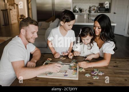 Lächelnde Eltern lösen Puzzle mit Kindern über Tisch zu Hause Stockfoto