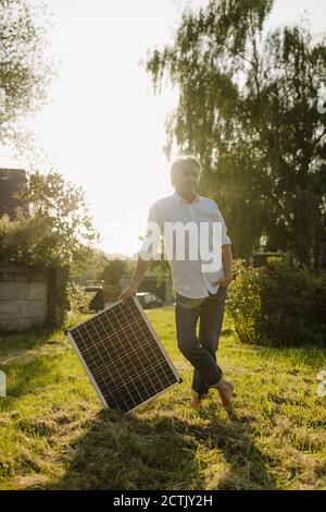 Mann hält Solarpanel gegen klaren Himmel im Hof Stockfoto