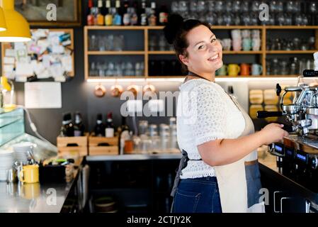 Lächelnde Barista, die beim Arbeiten an der Kaffeemaschine steht Café Stockfoto