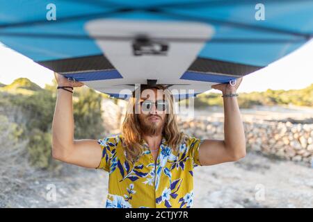 Junger Mann mit Paddelbrett am Strand während des Sonnenuntergangs Stockfoto