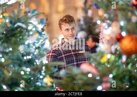 Junger Mann schaut auf beleuchteten Weihnachtsbaum und Lichter in Stadt Stockfoto