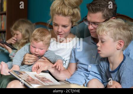 Familie schaut auf Fotoalbum, während sie im Wohnzimmer sitzt Stockfoto